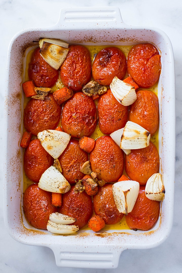 An overhead image of a baking sheet with roma tomatoes, garlic cloves and carrots in olive oil roasted in the oven and ready to be turned into Roasted Tomato Sauce.